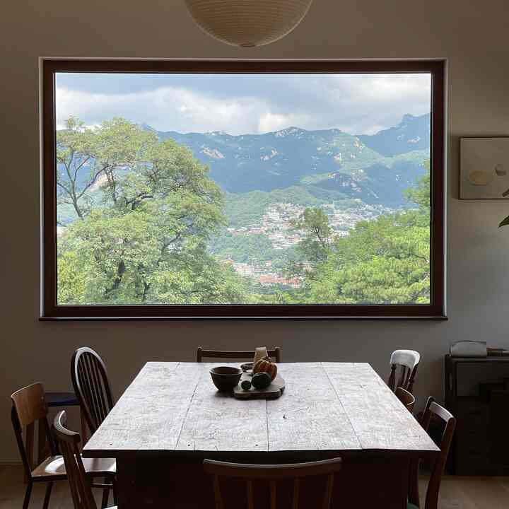 白と木目調が調和した4人用ヴィンテージダイニング、広い窓から北漢山の景色を楽しむ雰囲気のあるインテリア