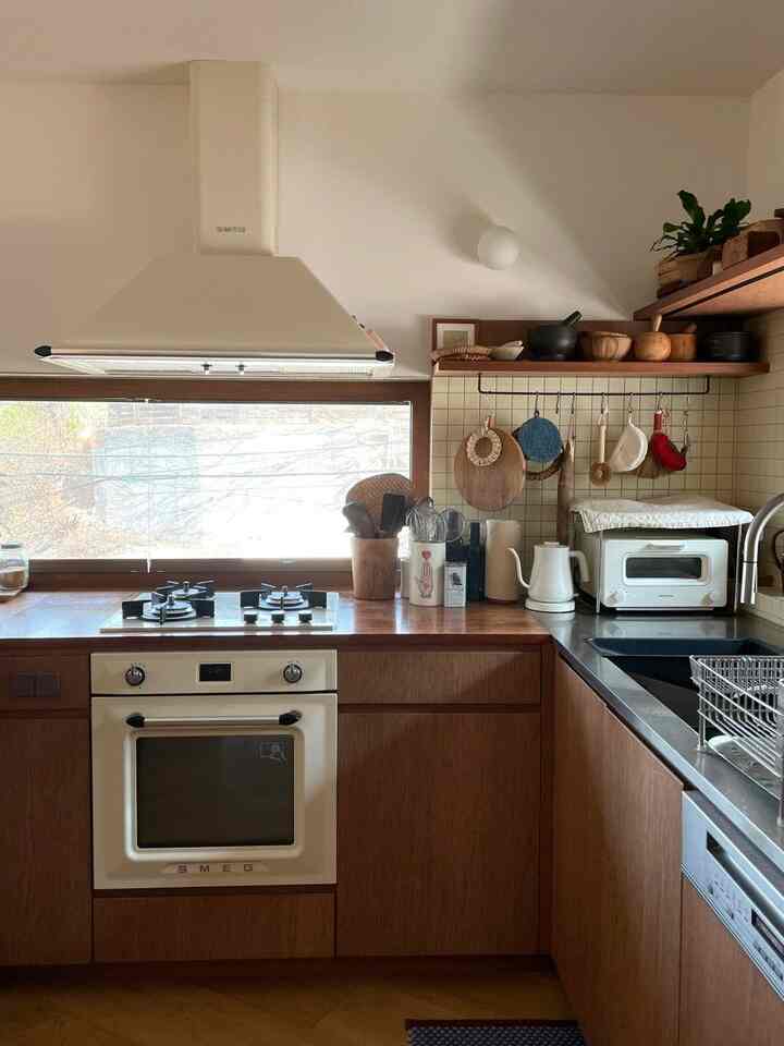 アイボリーの壁と木目調のキャビネットが調和したナチュラルスタイルのキッチン、中央にスメグのフードとオーブンが配置された印象的な空間