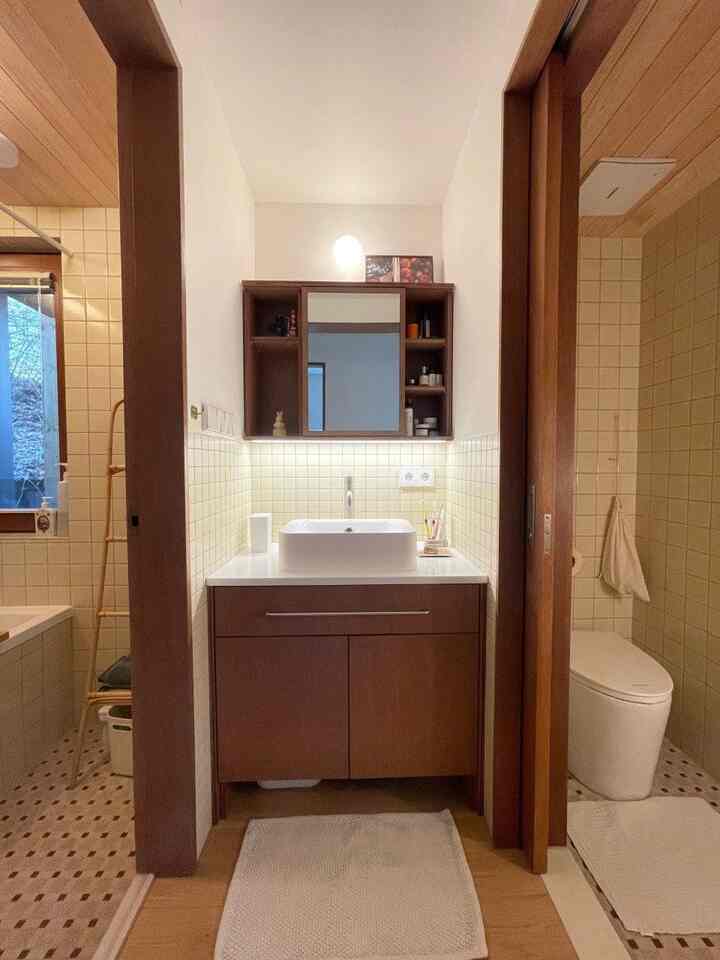 白と茶色のトーンのバスルーム、木製キャビネットと洗面台が配置された自然で落ち着いた雰囲気のインテリア