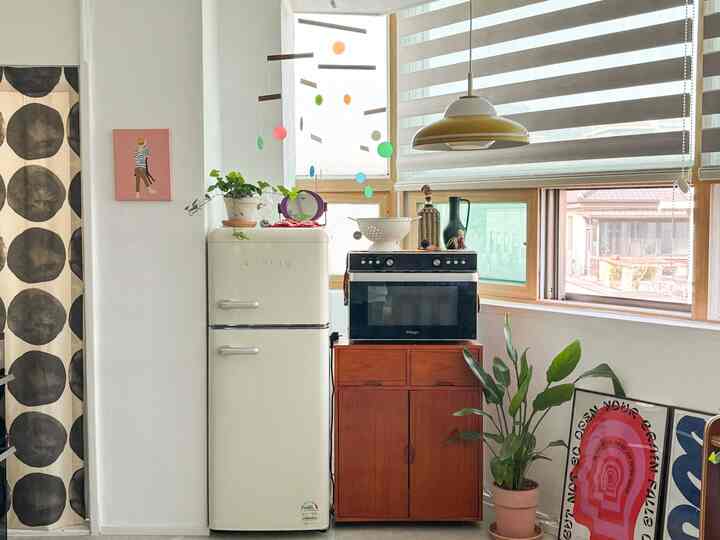明るく白を基調としたナチュラルウッド調のキッチン、レトロ冷蔵庫とキャビネット、カラフルなモビールと植物が調和した雰囲気のあるインテリア