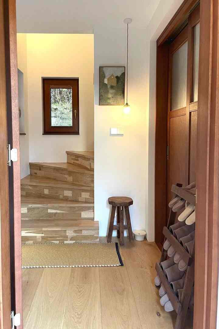暖かい木目調と白い壁の玄関、木製階段とスリッパ収納が配置された雰囲気のある空間