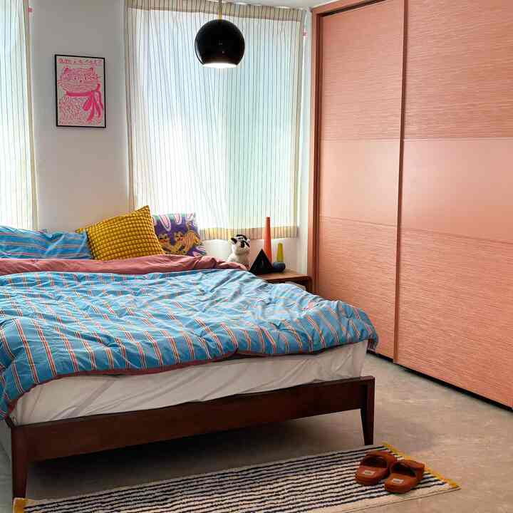 パステル調の寝室、青のストライプ掛け布団と木目調のクローゼット、白いカーテンが配置された雰囲気のある空間