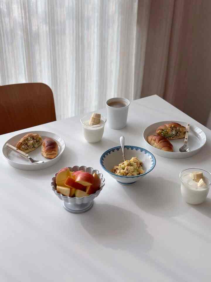 明るいホワイトトーンのリビングダイニングテーブルにさまざまな軽食と飲み物がきれいに盛り付けられた清潔感のある空間