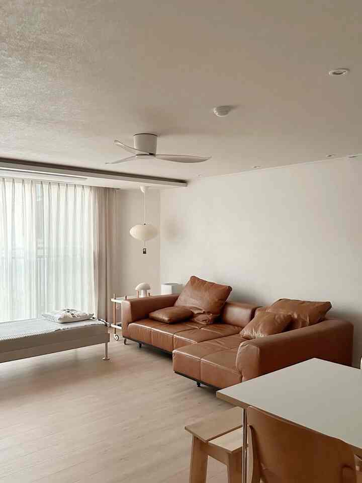 自然な色調のリビング、中央右にブラウンのコーナーソファ、窓際にベージュのカーテンが配置されたシンプルでモダンな空間