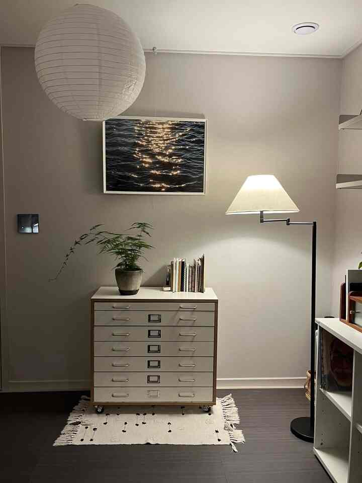 白とナチュラルカラーの空間にファイリングキャビネット、フロアランプ、ポスターが配置された落ち着いた収納スペース