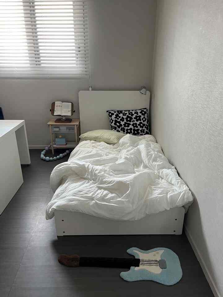 ホワイトトーンの狭い寝室、ホワイトベッドと木製ナイトテーブル、ギター形ラグが配置されたすっきりとした空間