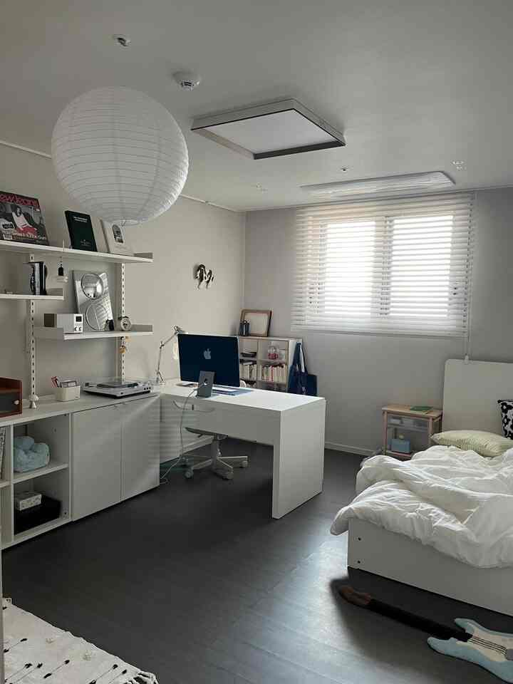 ホワイトとウッドトーンが調和した一人暮らし向けのコンパクトな部屋、実用的なデスクとベッドが配置されたモダンな空間