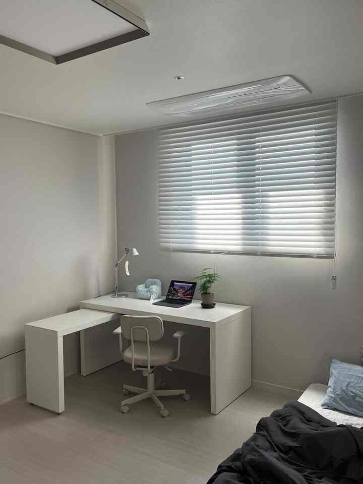 白を基調とした寝室兼ホームオフィス空間、シンプルな白いデスクとオフィスチェア、ブラインド、ベッドが配置された落ち着いたインテリア