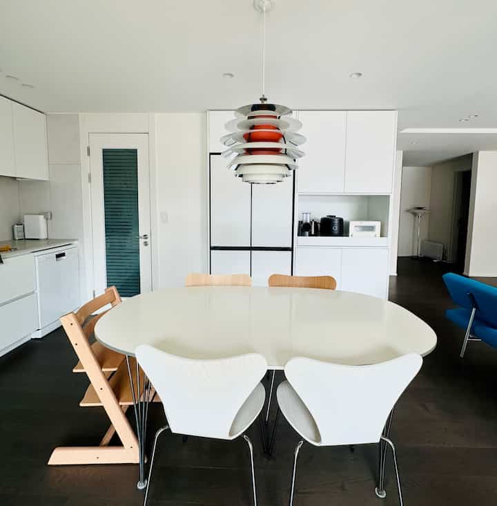 白と木目調が調和したキッチンとダイニングルーム、ルイスポールセン照明とフリッツハンセンの椅子が配置されたモダンな空間