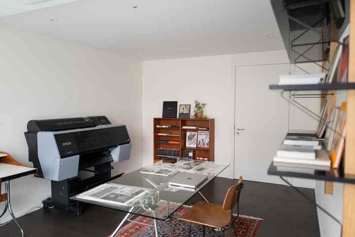 白い壁と天井が際立つホームオフィス空間。ガラス製の机、大型のエプソンプリンター、木製収納が配置された整ったワークスペース