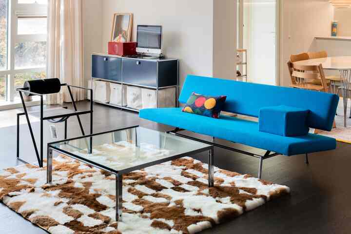 明るいブルーのソファが中心の白い壁のリビング、モダンでナチュラルなスタイルのコーヒーテーブルとアームチェアが配置された印象的な空間