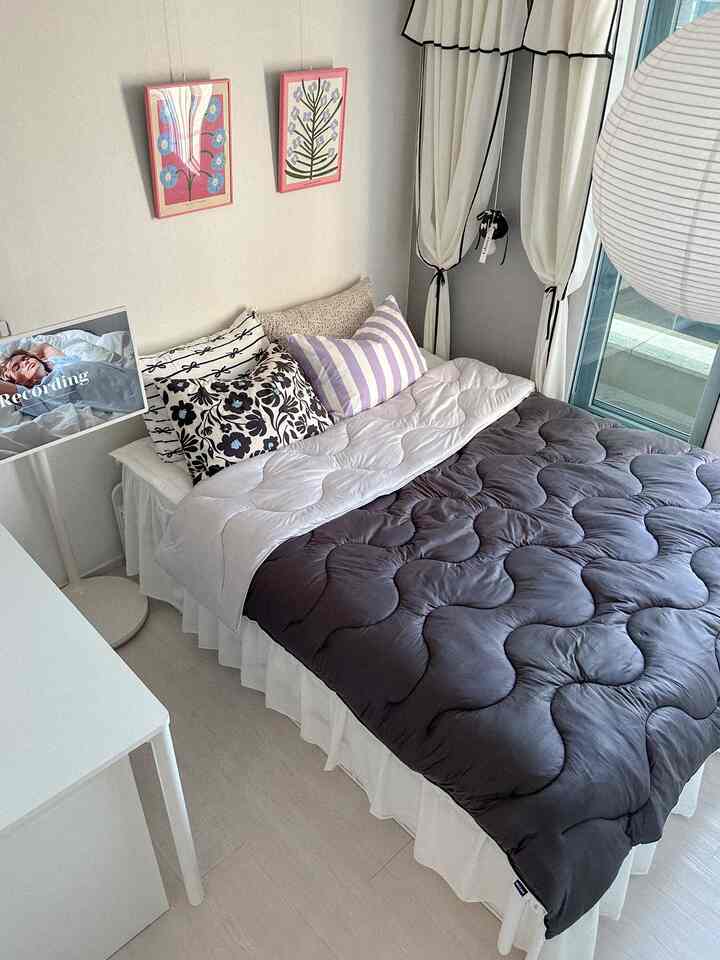 白とグレーのトーンの寝室、柄入りの枕とフリルのベッドスカートが調和したナチュラルモダンな雰囲気のインテリア