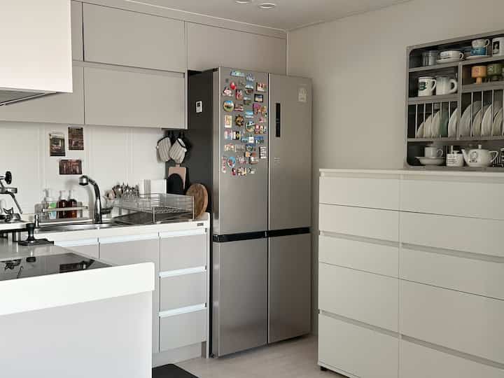 白とグレーの色調のキッチン、大型冷蔵庫と整然とした収納キャビネットが配置されたモダンで清潔感のある空間