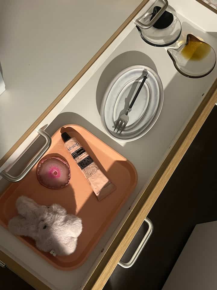 白と茶色のトーンの引き出しの内部、ピンクのトレイと皿がきれいに配置された落ち着いた空間