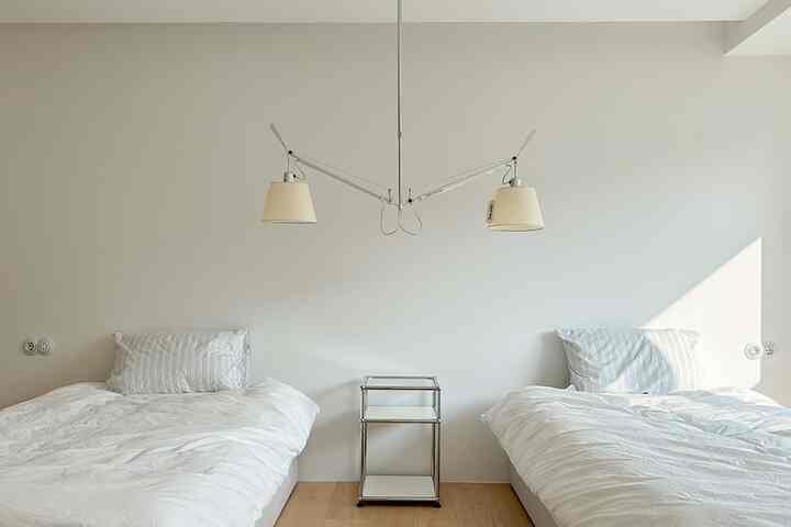 白い壁と木目調の床が特徴的な寝室、二つのベッドとナイトテーブル、ツインの照明が落ち着いた印象の空間