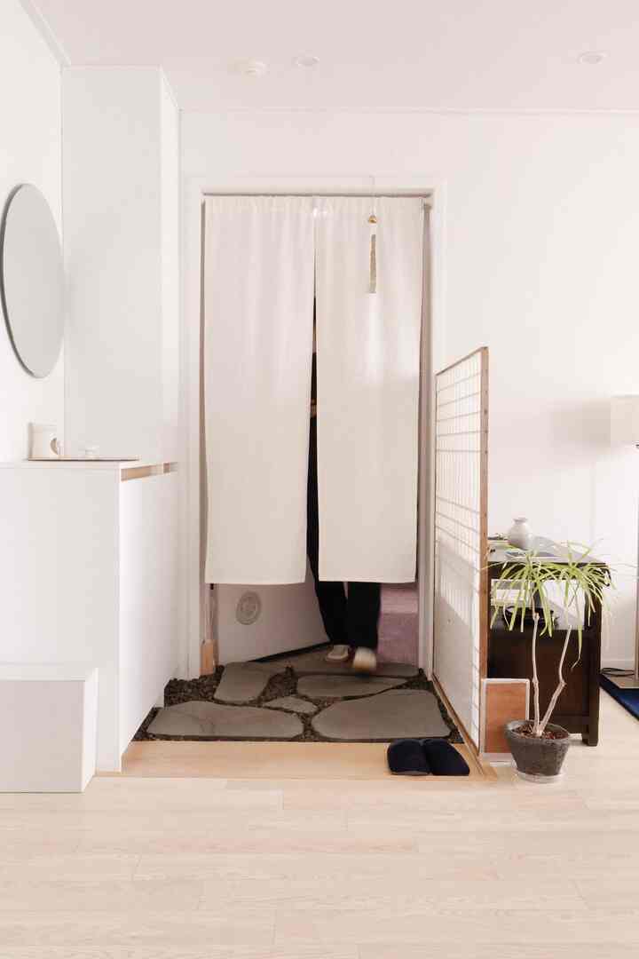 明るい木目調の床と白い壁が調和する中扉のないモダンな玄関、自然な石の踏み石と丸い鏡が配置された空間