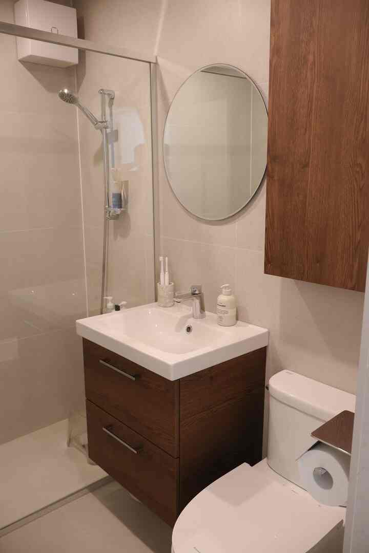 白と茶色のトーンのバスルーム、洗面台と丸い鏡、シャワースペースが配置された清潔感のあるモダンなインテリア