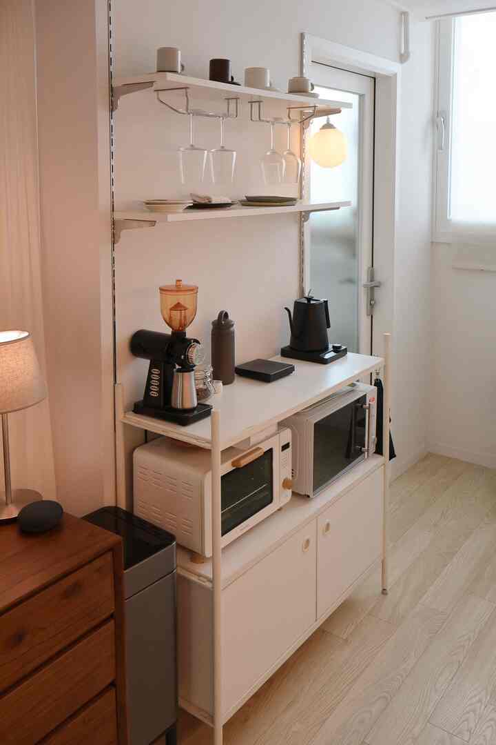 白と木目調のリビングルーム、キッチン収納とコーヒー器具が配置された清潔でナチュラルなインテリア