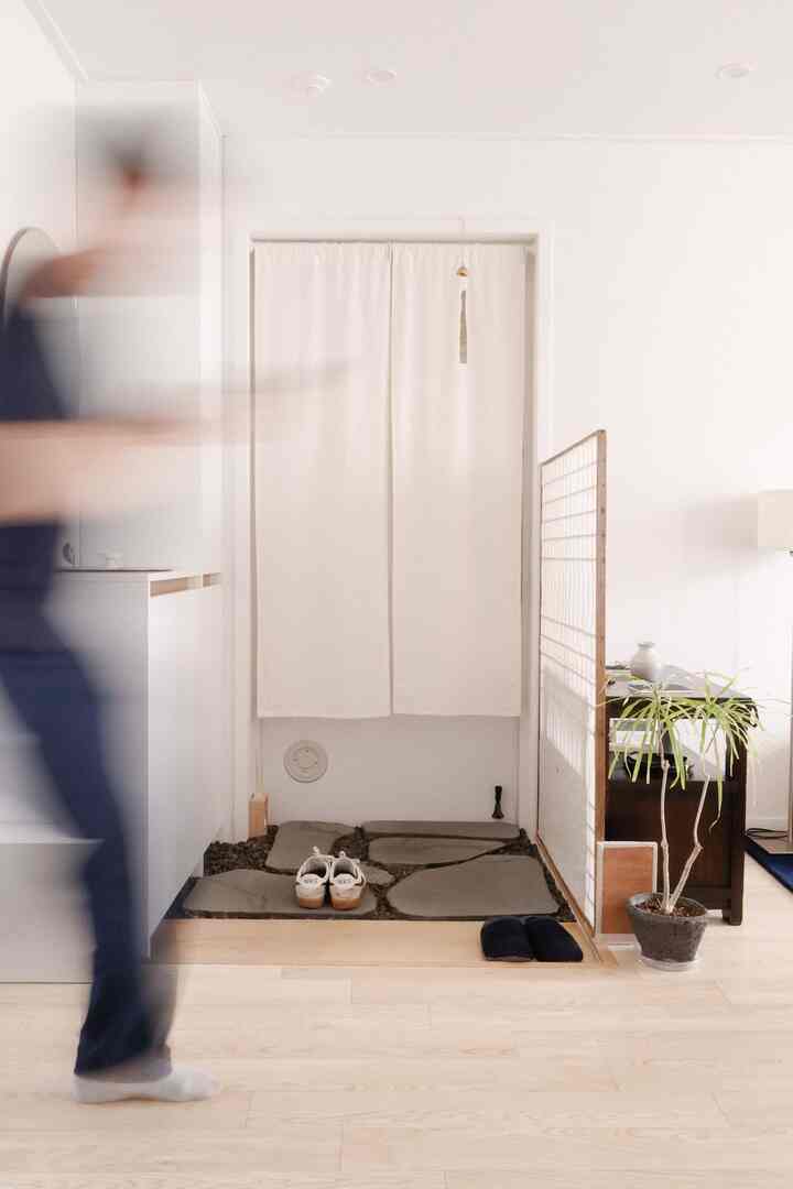 明るい木目調の床と白い壁とカーテンがある玄関、特徴的な敷石と間仕切り、植物が配された自然な雰囲気のインテリア