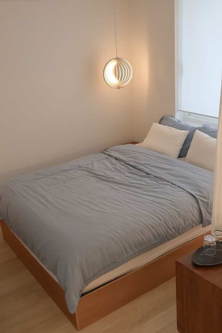 ベージュの壁と木目調のベッドが配置された、シンプルでナチュラルな夫婦の寝室のインテリア