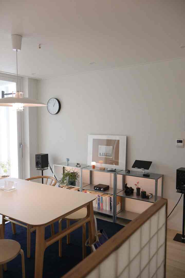 白と木目調が調和したリビング兼ダイニングルーム、テーブルと椅子、棚が整然と配置されたモダンな空間