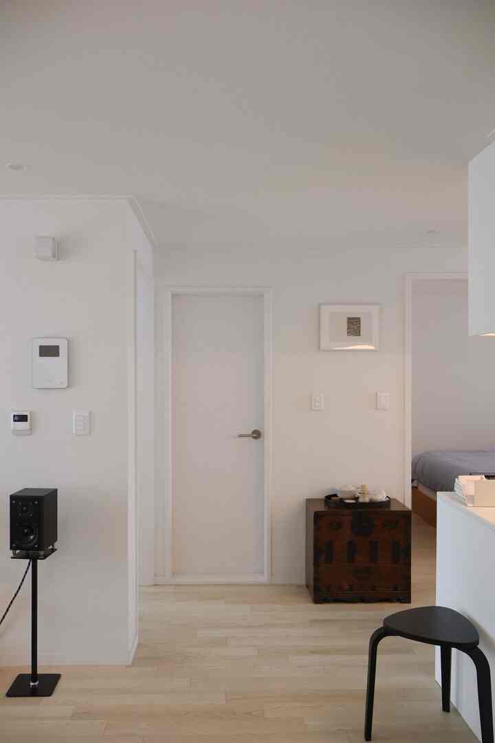 白とナチュラルカラーの小型アパートのリビングルームと寝室入口、ミニマルな家具でモダンな印象の空間