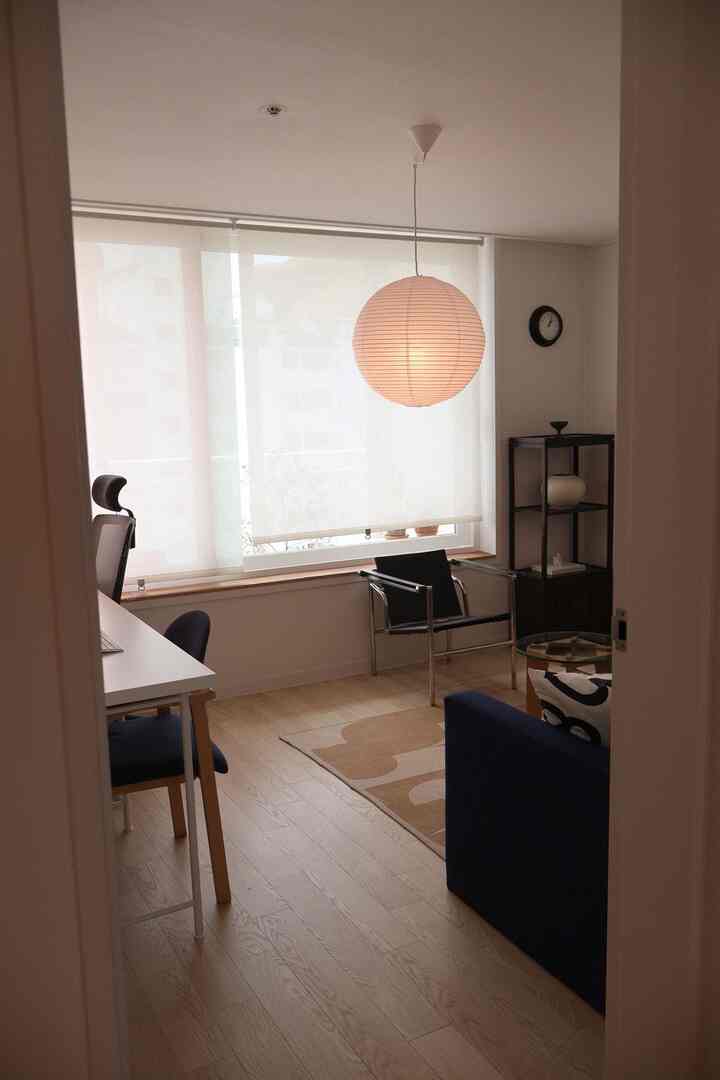 ライトブラウンの木製フロアと白い壁のホームオフィス空間、ネイビーブルーのソファとミニマルな家具が配置された清潔感のあるインテリア