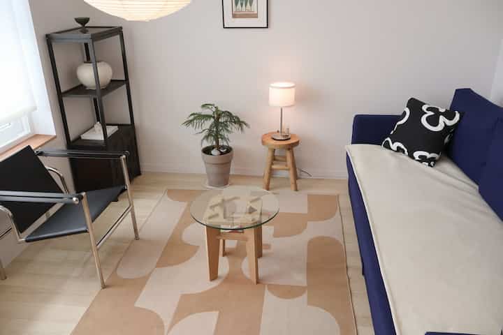 ネイビーブルーのソファとシンプルな鉄製チェア、ウッドサイドテーブルが配置されたミニマルなリビング