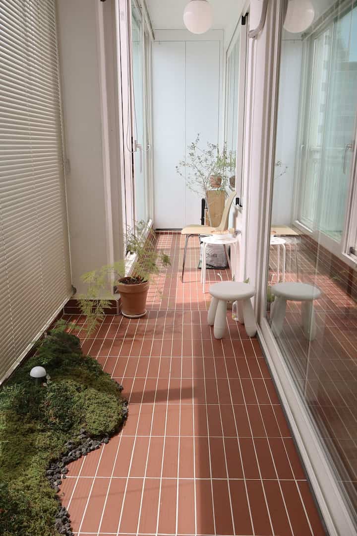 温かみのあるテラコッタタイルの床と自然な植物が配された明るいベランダ空間