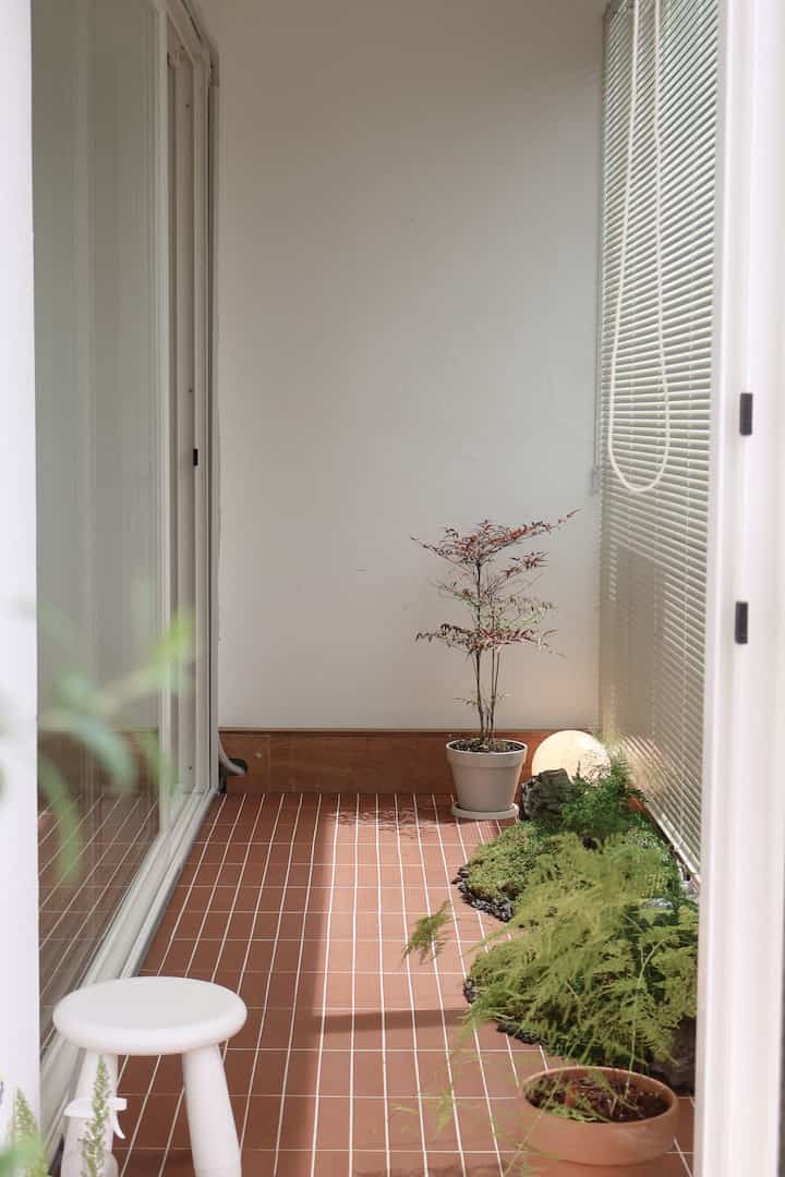 暖かいテラコッタの床と白いブラインドがあるベランダ、鉢植えとスツールが配された自然で落ち着いた雰囲気のインテリア
