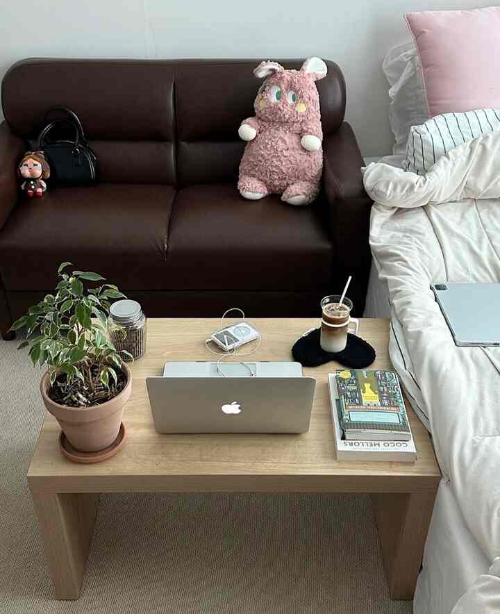 ナチュラルな木目調とホワイトカラーの寝室、木製テーブルとブラウンソファが配置された温かみのある空間