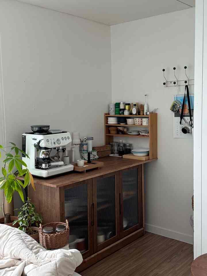 木目調の家具と白い壁が調和した居心地の良いおうちカフェ空間、コーヒーマシンと植物がアクセントのミニマルインテリア