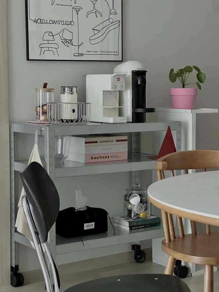 白い壁とグレーの金属製キッチンワゴンにコーヒーマシンや小物が配置されたミッドセンチュリーモダン風の寝室のインテリア