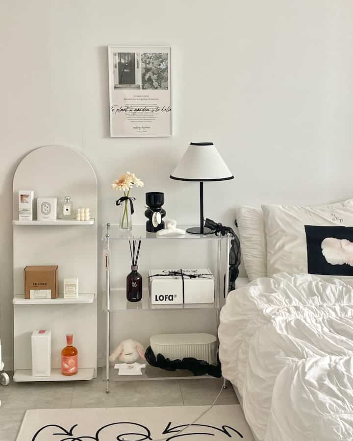 白とベージュの寝室、ベッドと透明な棚、テーブルランプ、花瓶が配置されたミニマルで自然な雰囲気のインテリア