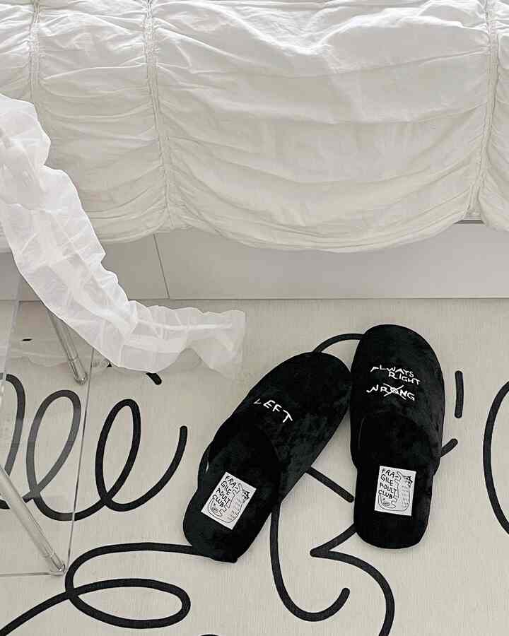 明るいホワイトトーンの寝室、白いベッドカバーと黒い曲線模様のラグの上に黒いスリッパが置かれた雰囲気のあるインテリア