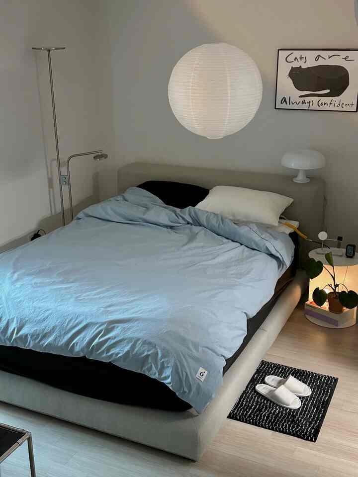 明るいグレーと黒のトーンの寝室、ミニマルなベッド、白と黒の枕、猫のポスターが配置された落ち着いた空間