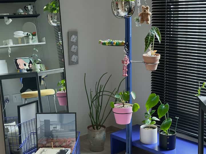 ナチュラルな色調の寝室、多様な植物と青いプラントスタンドが配置された雰囲気のある個人空間