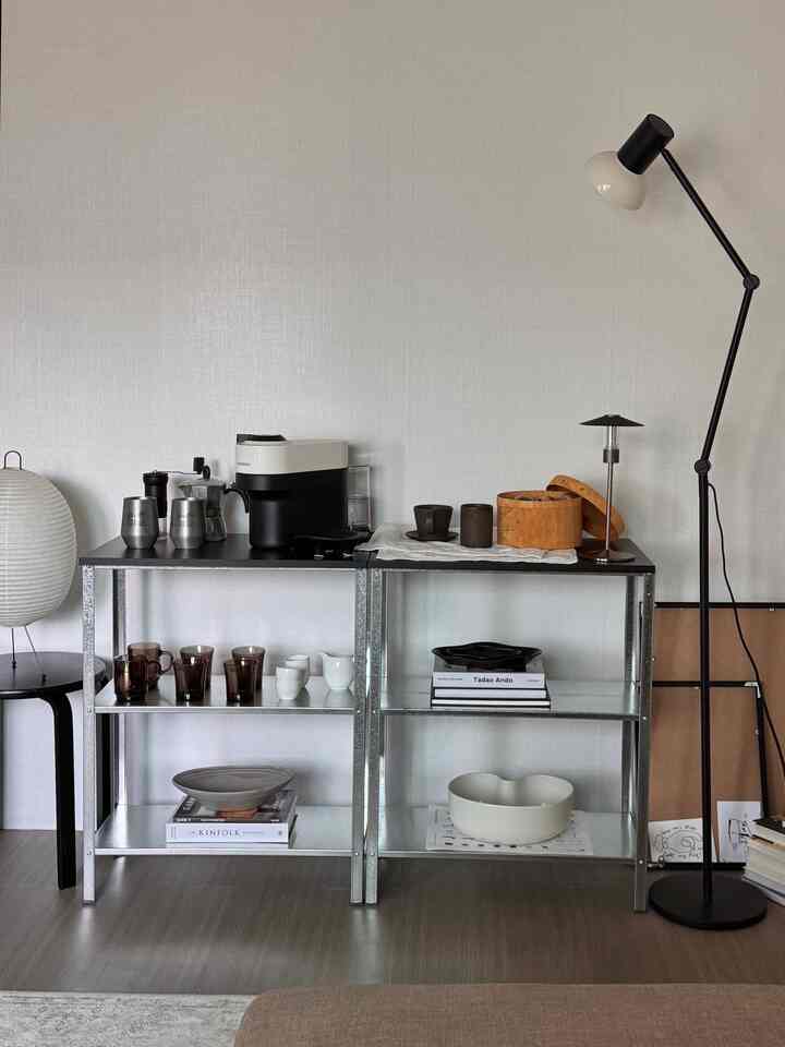 シルバーのメタル棚と黒のフロアランプがあるミニマルで清潔感のあるリビングルーム