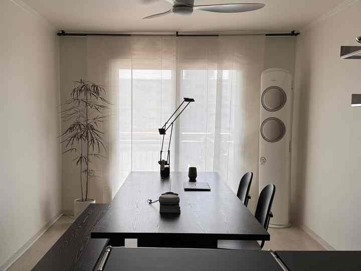 白い壁とカーテン、黒いテーブルと椅子が配置されたモダンでコンパクトなホームオフィス空間