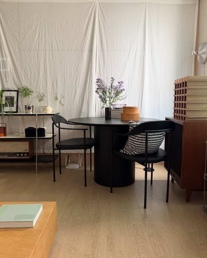 ナチュラルな木目調の床と黒いダイニングテーブル、椅子が配置されたシンプルでモダンなリビング空間