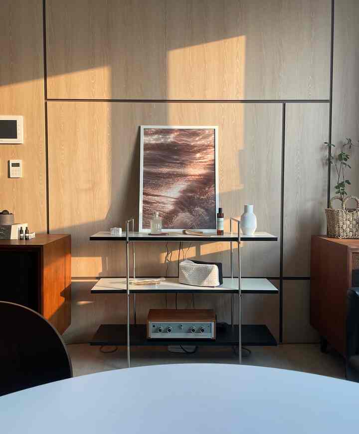 温かみのある木目調のリビング、中央の棚にアートポスターやディフューザー、花瓶が配置された自然な雰囲気のインテリア