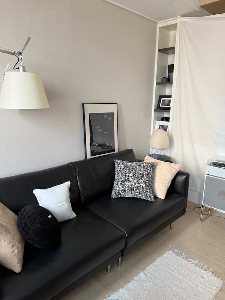 ブラックレザーソファとナチュラルトーンのワンルームリビング、大きなカーテンで空間を仕切るモダンで落ち着いた印象のインテリア