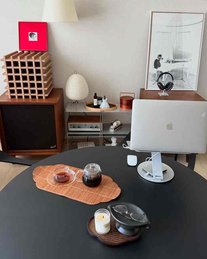 ウッドトーンとヴィンテージスタイルが調和したリビング、モダンな雰囲気の中、黒い丸テーブルにホームカフェ用品とノートパソコンが配置された印象的な空間