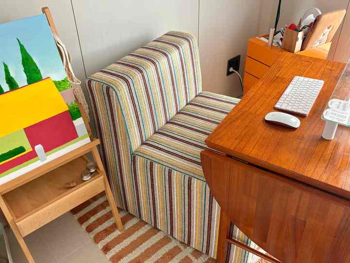 ナチュラルカラーのホームオフィス、ストライプのソファと木製デスク、絵画が配置された雰囲気のある作業空間
