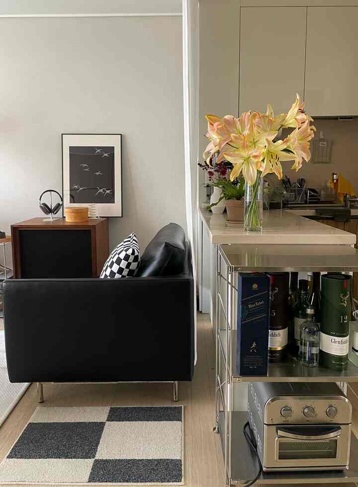 モダンスタイルのリビングとキッチン、黒いレザーソファとスチール棚、リネンカーテンが調和した洗練されたインテリア