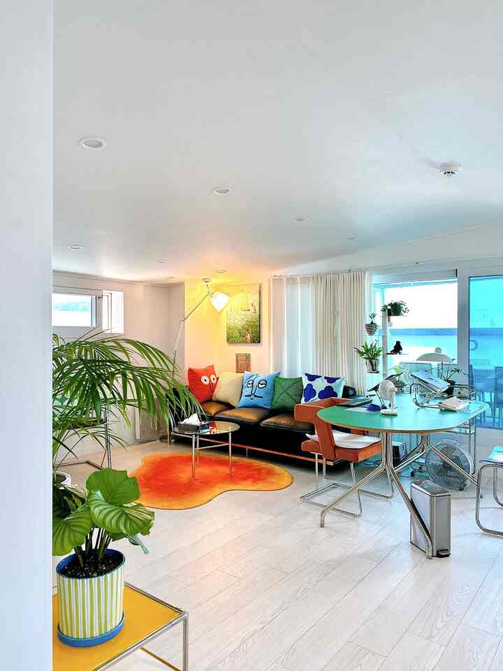 白を基調としたミッドセンチュリーモダンの家具とオレンジのラグが配置された明るく落ち着いたリビング