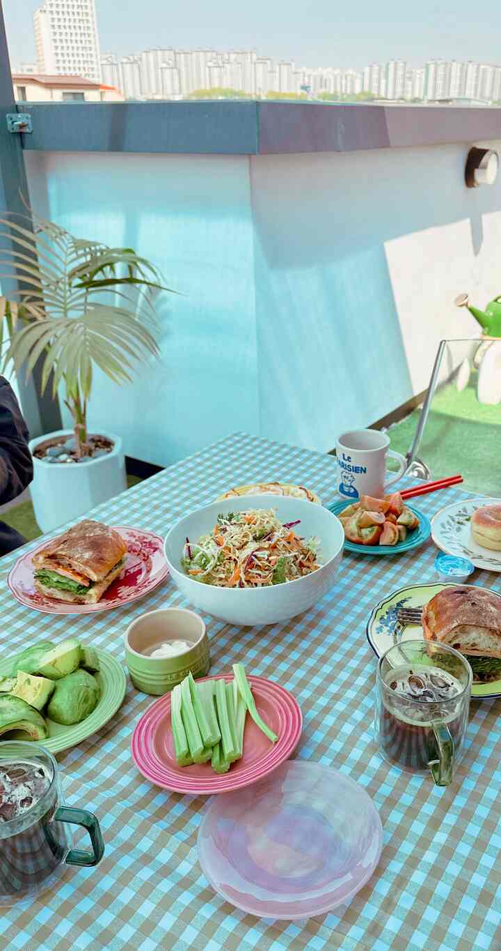 パステル調のチェック柄テーブルクロスのあるテラス、多彩なかわいい食器が配置された、明るく温かみのある家族のブランチ空間