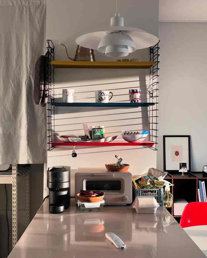 白い壁とカラフルなトマドの棚がある居心地の良いキッチン、コーヒーマシンとオーブントースターが置かれたシンプルな空間