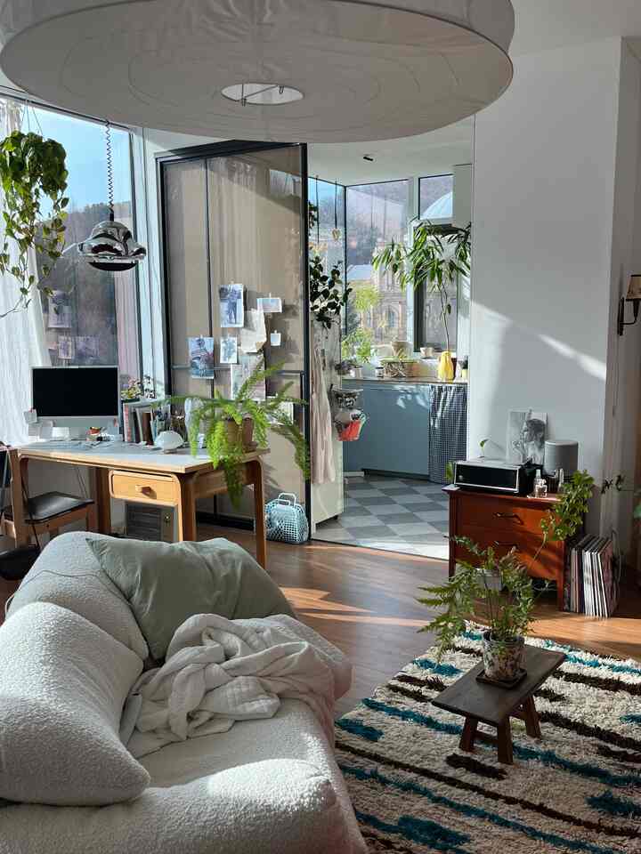 明るい白とナチュラルウッドトーンのリビングとホームオフィス空間、青いキッチンキャビネットと植物が調和したナチュラルモダンなインテリア