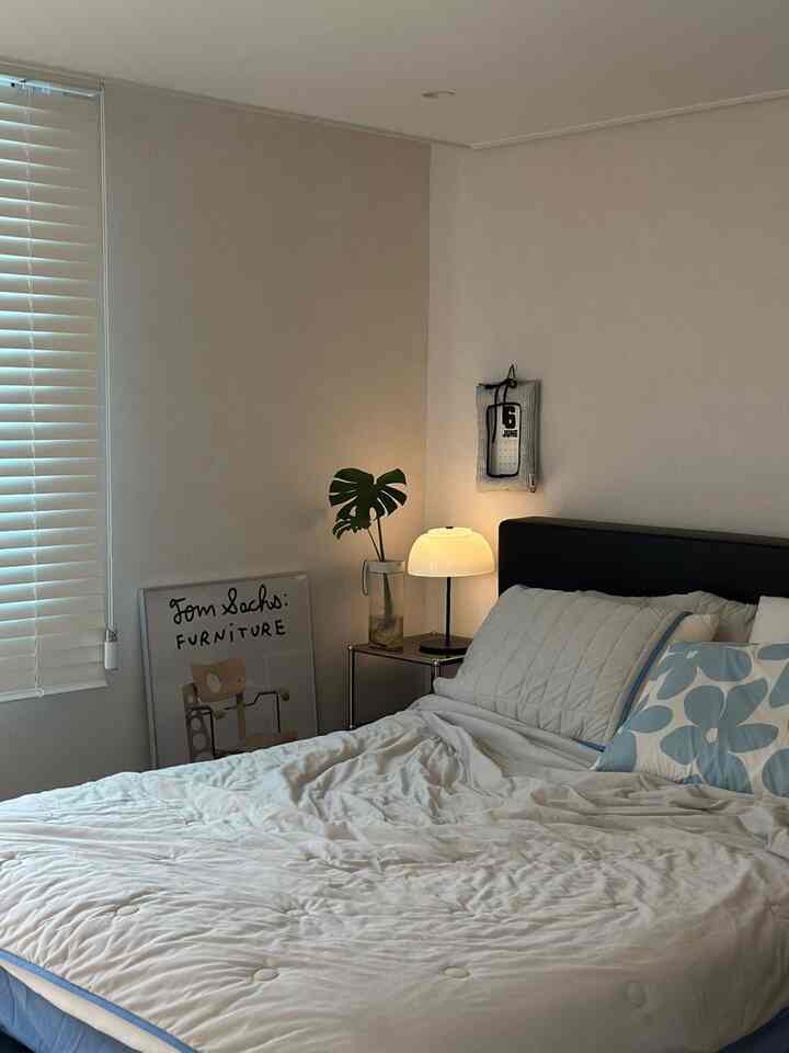 柔らかなナチュラルカラーの寝室、白い寝具とブラインド、テーブルランプが調和した落ち着いた空間